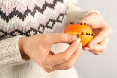 Woman decorating fresh tangerine with cloves, closeup. Making Christmas pomander ball