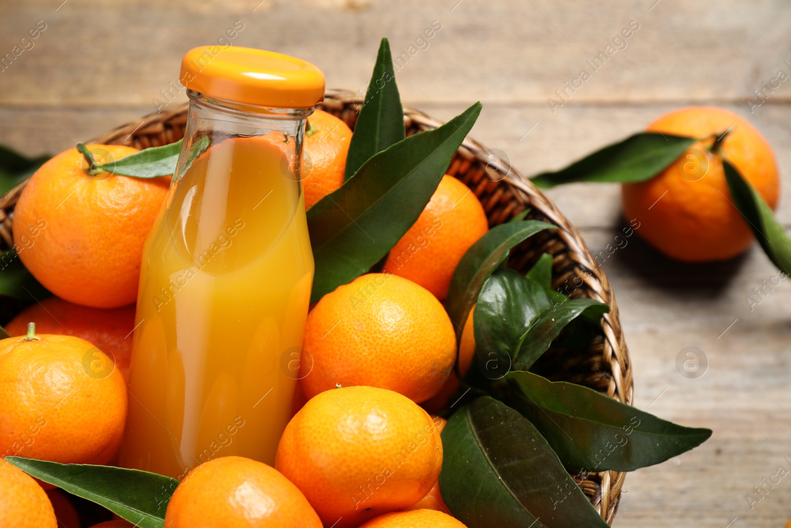 Photo of Basket with fresh tangerines and bottle of juice on wooden table, closeup