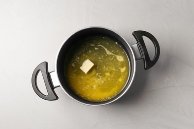 Pot with melting butter on grey table, top view