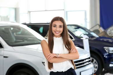 Photo of Young saleswoman standing in modern car salon