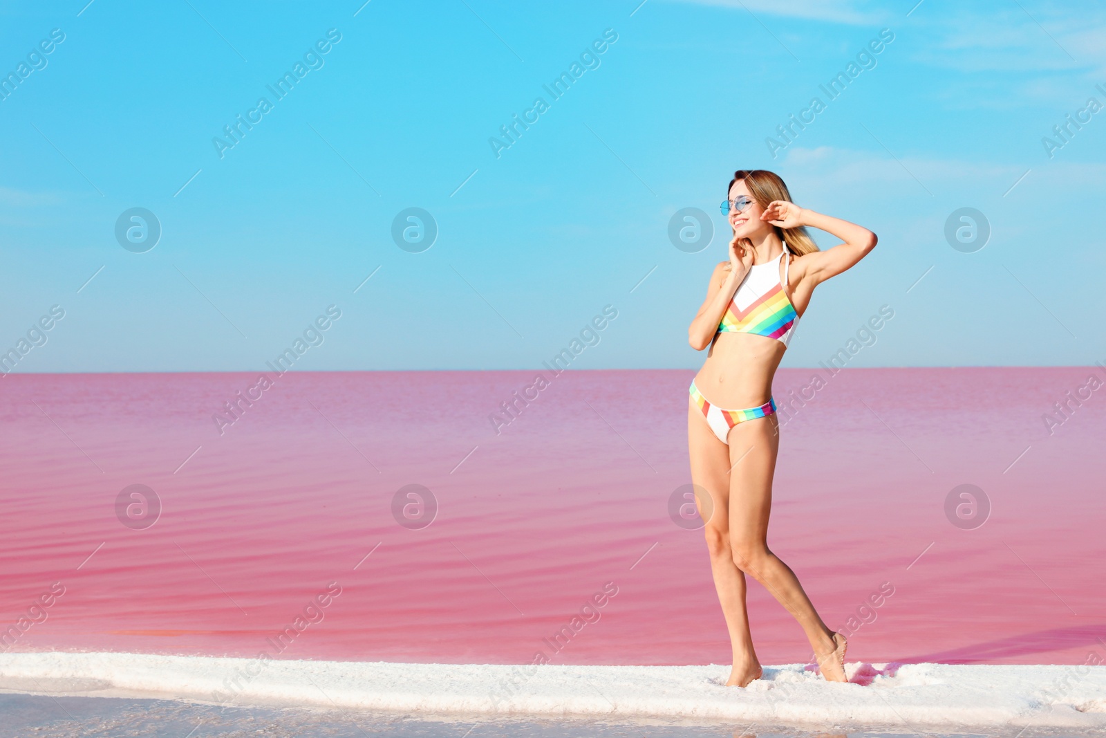 Photo of Beautiful woman in swimsuit standing near pink lake on sunny day