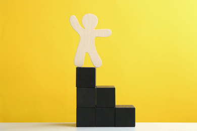 Wooden human figure on top of block staircase against yellow background. Career promotion concept
