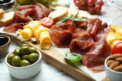 Photo of Charcuterie board. Delicious bresaola, olives, tomato, cheese and almond on white marble table, closeup