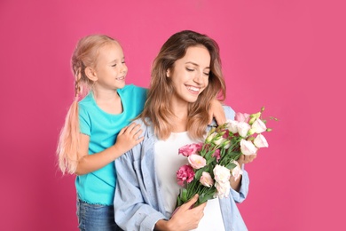 Photo of Little daughter congratulating her mom on pink background. Happy Mother's Day