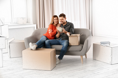 Image of Couple unpacking cardboard box while resting on sofa in their new house 