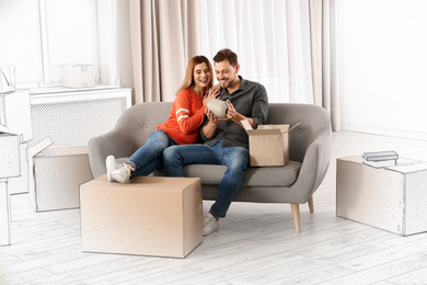 Couple unpacking cardboard box while resting on sofa in their new house 