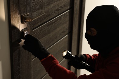 Thief with flashlight breaking foreign door's lock in hall. Burglary