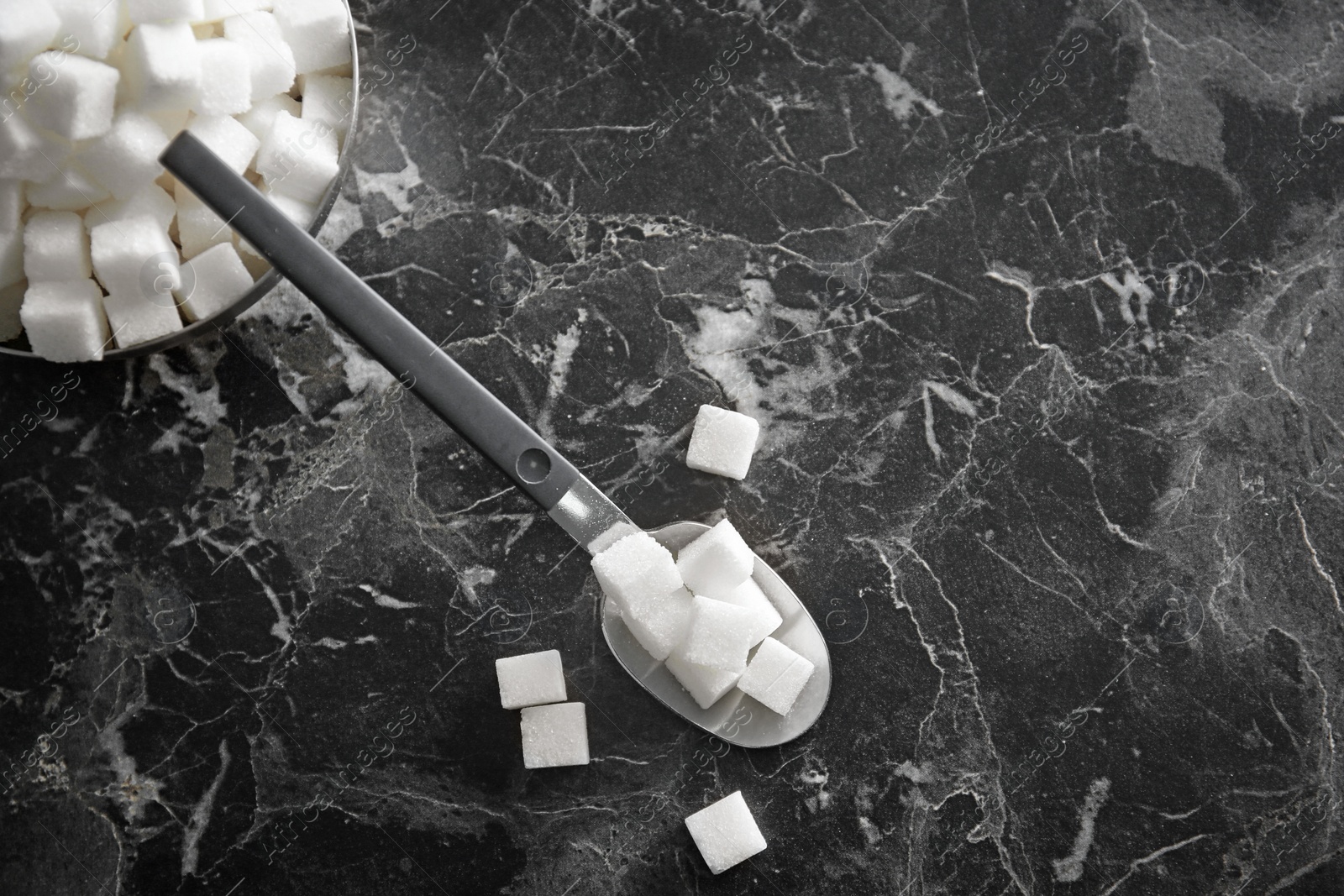 Photo of Bowl and spoon with refined sugar cubes on dark grey background