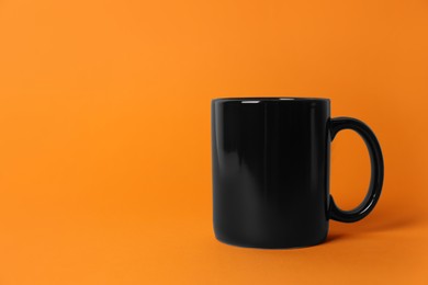 Photo of One black ceramic mug on orange background. Space for text
