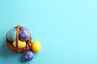 Wicker basket with painted Easter eggs on color background, top view. Space for text