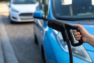 Photo of Woman holding power supply cable at electric vehicle charging station, closeup