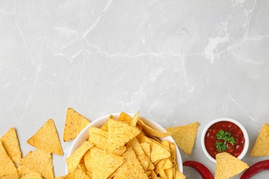Photo of Mexican nacho chips with sauce on grey marble background, flat lay. Space for text