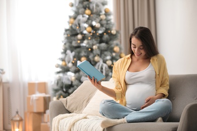 Happy pregnant woman with book in living room decorated for Christmas. Expecting baby