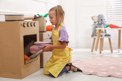 Little girl playing with toy cardboard oven at home
