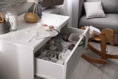 Modern open chest of drawers with baby clothes and accessories in room