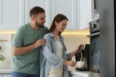 Photo of Happy couple preparing fresh aromatic coffee with modern machine in kitchen