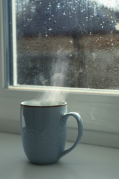 Image of Cup of hot drink near window on rainy day