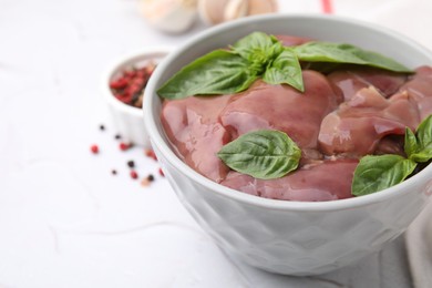 Photo of Bowl with raw chicken liver and basil on white textured table, closeup. Space for text
