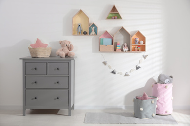 Photo of Cute children's room with house shaped shelves and chest of drawers. Interior design
