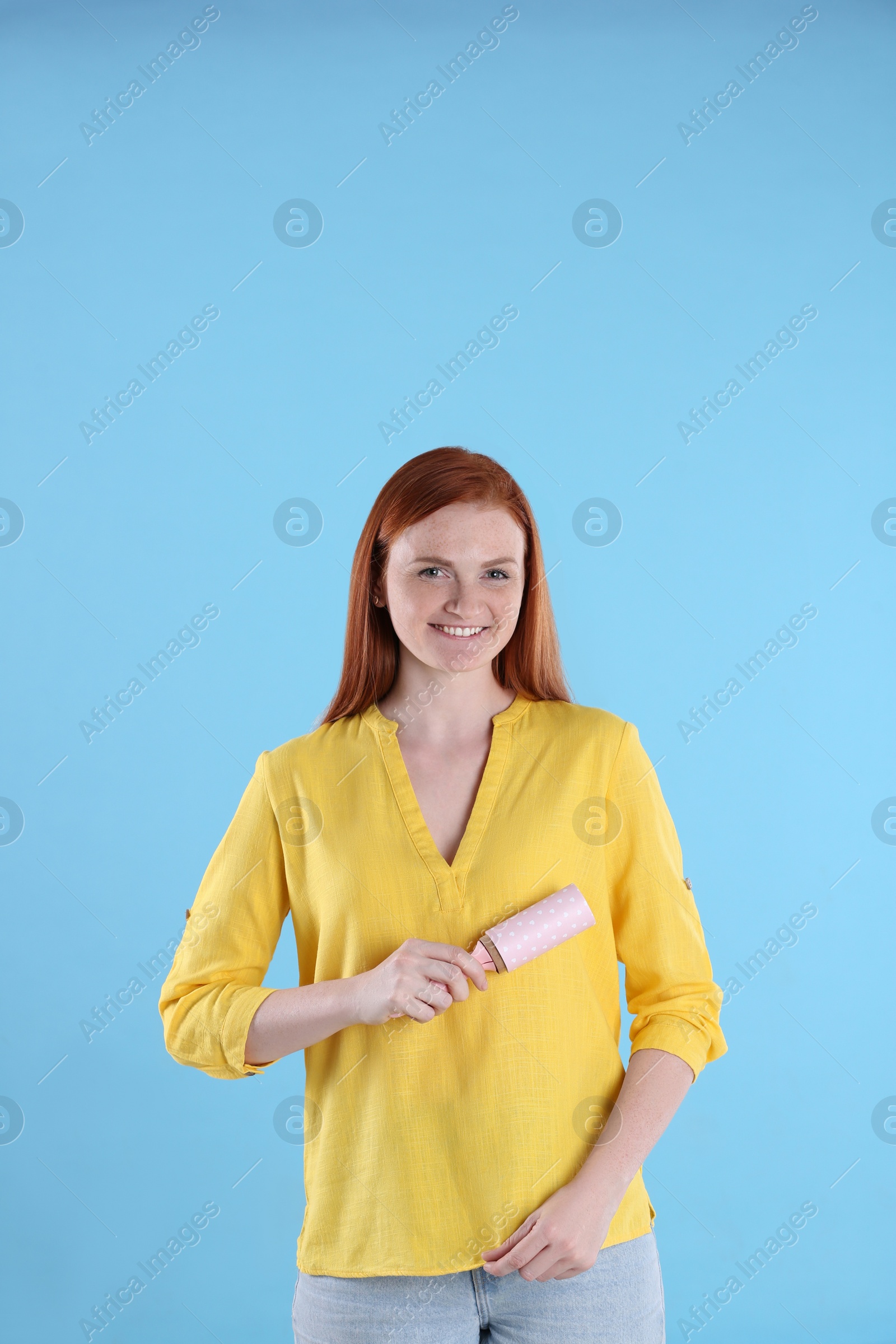 Photo of Young woman cleaning clothes with lint roller on light blue background