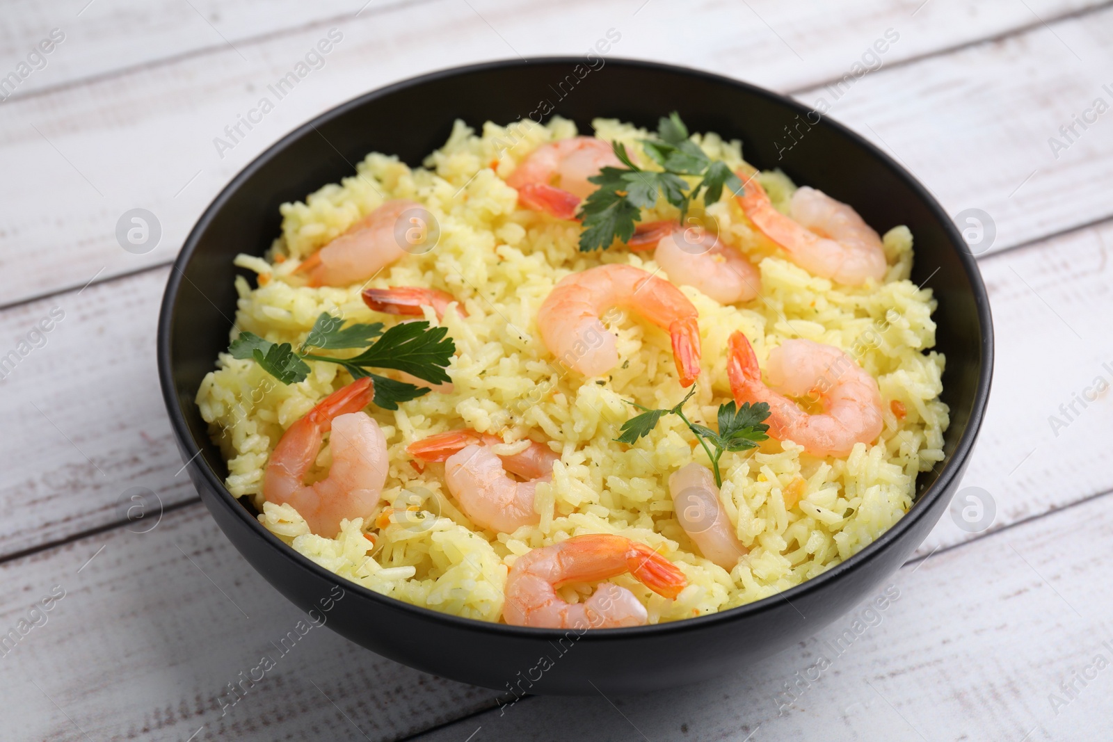 Photo of Delicious risotto with shrimps and parsley in bowl on white wooden table, closeup