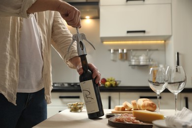 Man opening wine bottle with corkscrew at table indoors, closeup