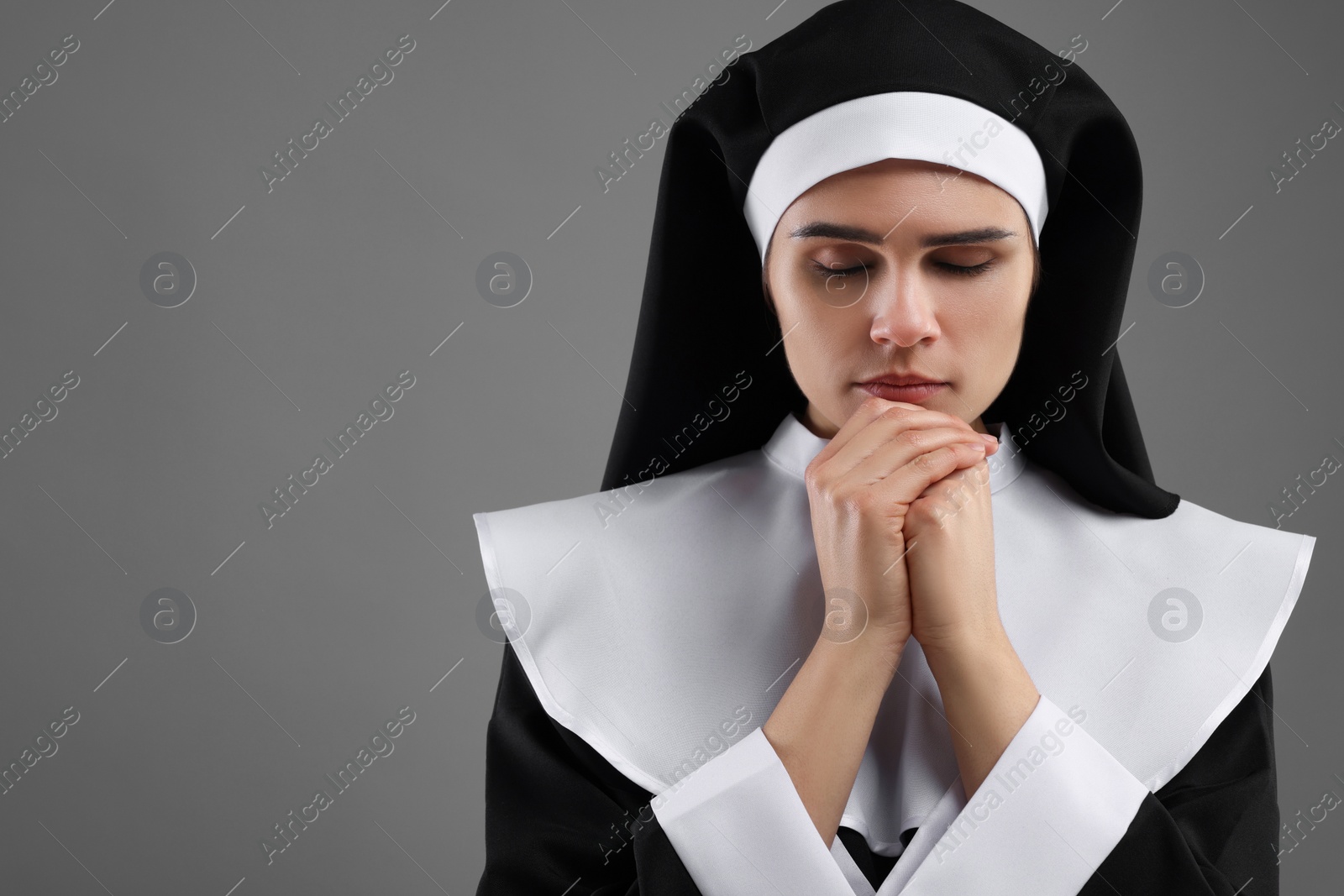 Photo of Nun with clasped hands praying to God on grey background. Space for text