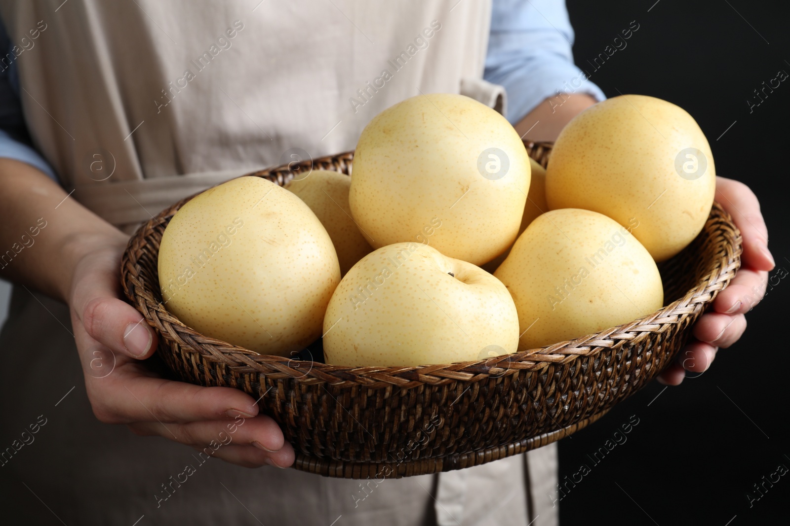 Photo of Woman holding wicker bowl ripe apple pears on black background, closeup