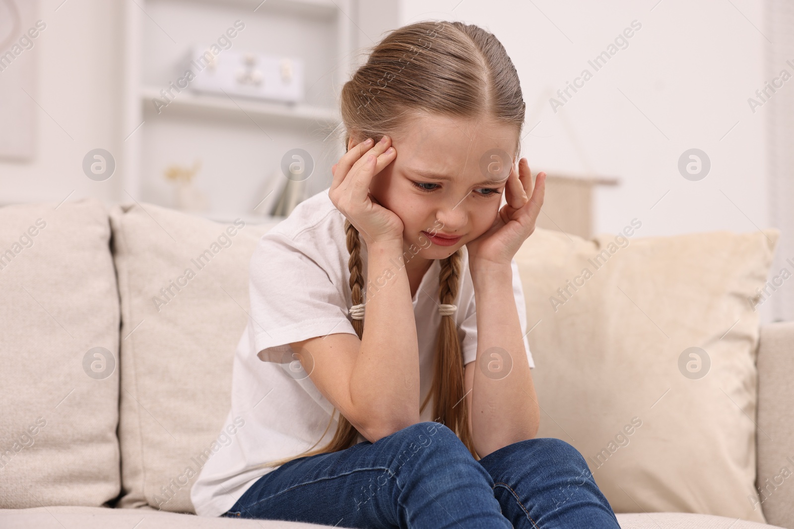 Photo of Little girl suffering from headache on sofa indoors