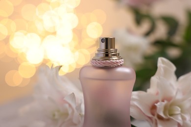 Photo of Bottle of perfume and beautiful lily flowers against beige background with blurred lights, closeup