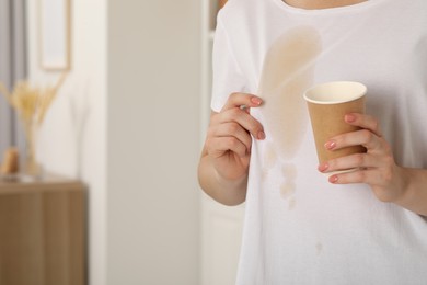 Photo of Woman showing stain from coffee on her shirt indoors, closeup. Space for text