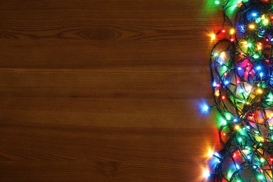 Photo of Colorful Christmas lights on wooden table, top view. Space for text