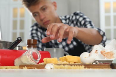 Photo of Upset man with many dirty dishware, utensils and food leftovers on table in messy kitchen, selective focus