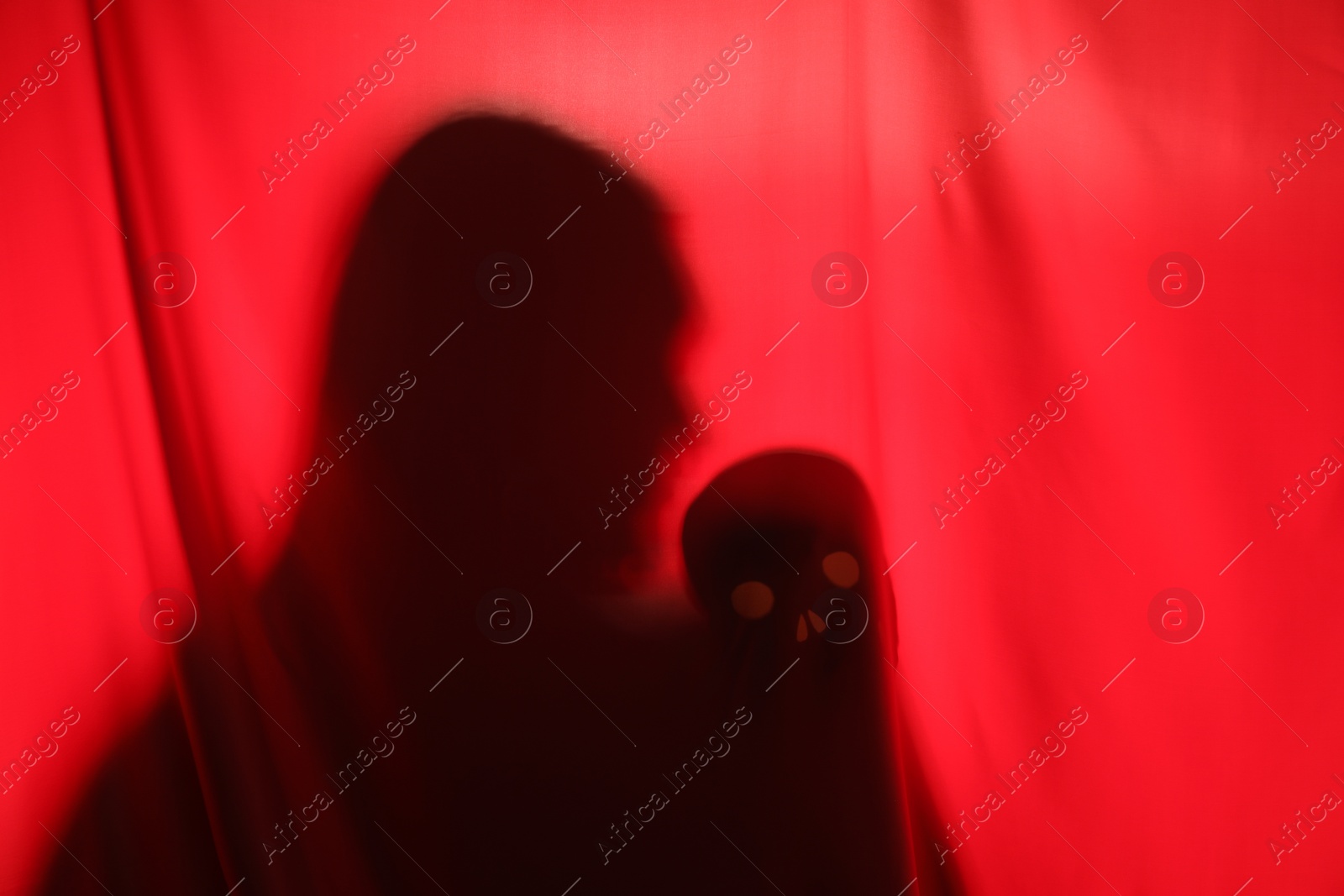 Photo of Silhouette of creepy ghost with skull behind red cloth, space for text