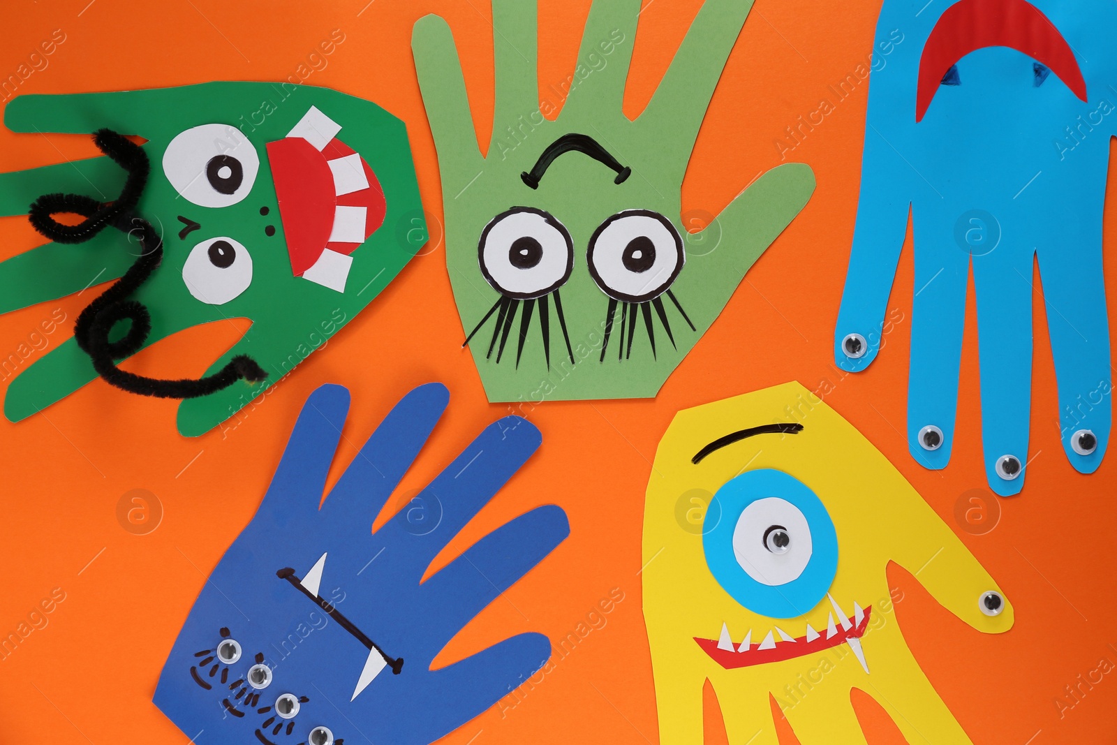 Photo of Funny hand shaped monsters on orange background, flat lay. Halloween decoration