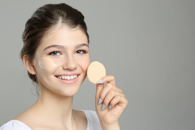 Photo of Beautiful girl with foundation smear on her face holding sponge against grey background. Space for text