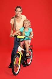 Young mother teaching daughter to ride bicycle on red background