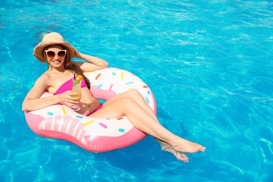 Young woman with cocktail in pool on sunny day