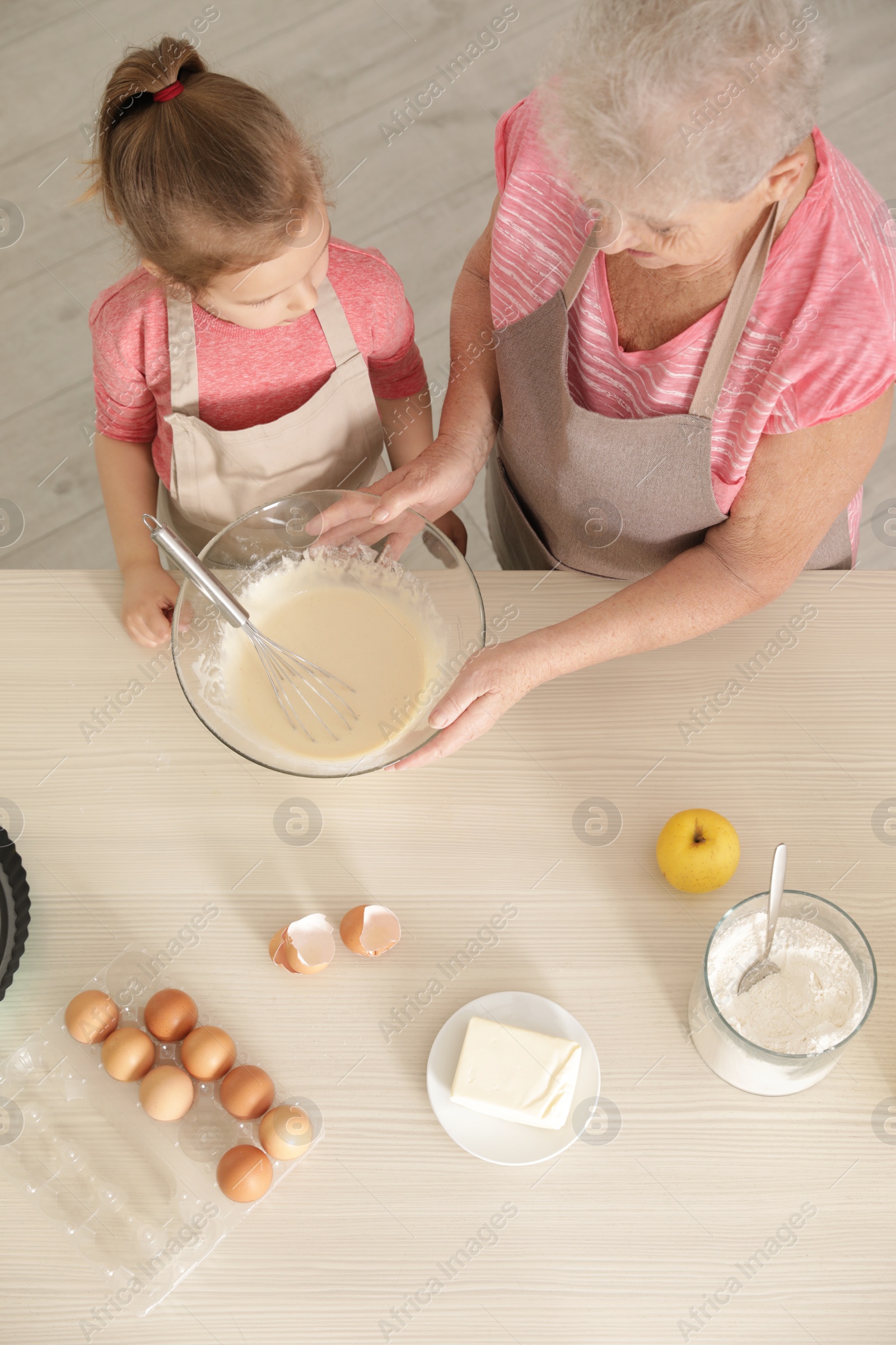 Photo of Little girl and her grandmother cooking at table with products, top view