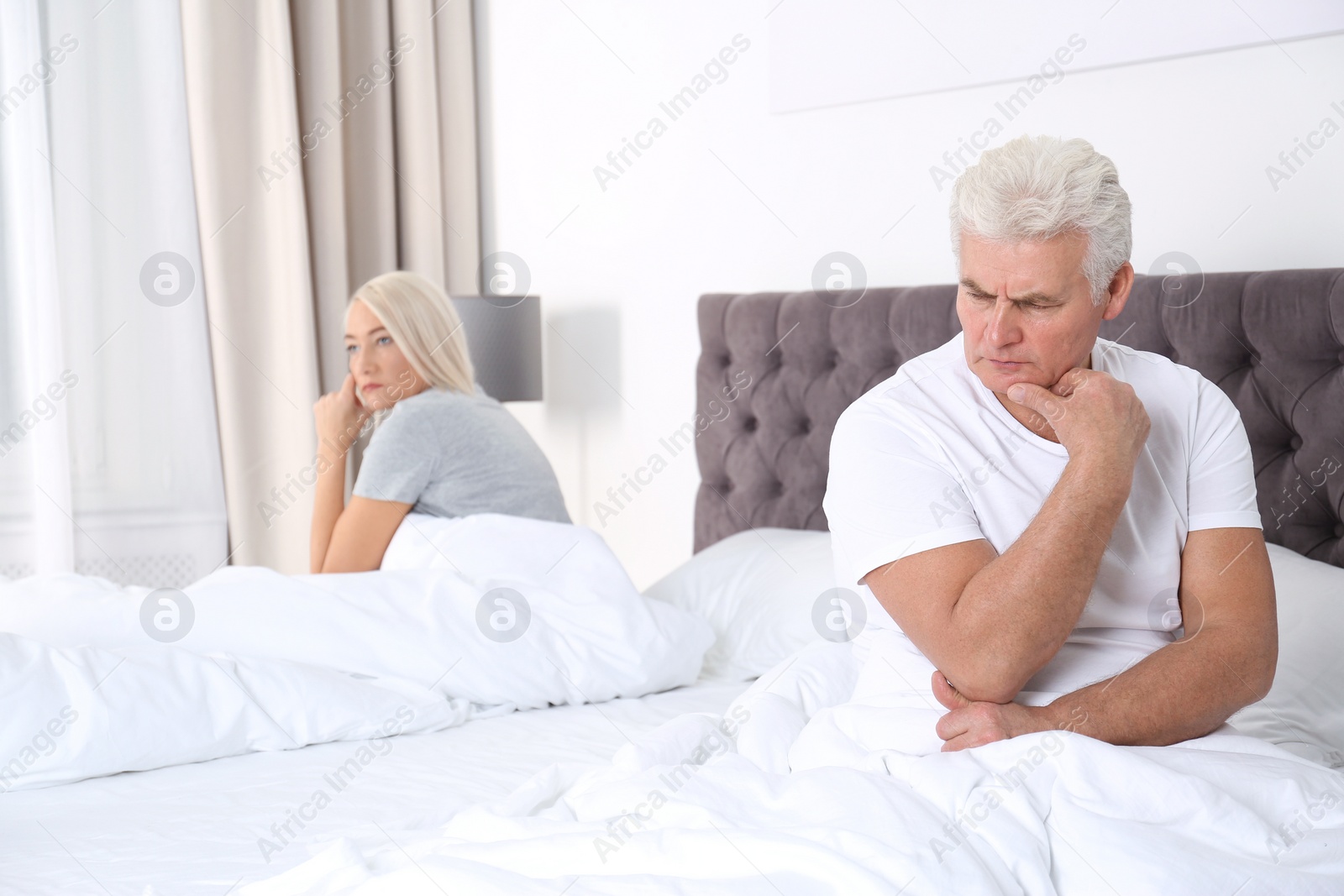 Photo of Upset mature couple with relationship problems sitting on bed at home