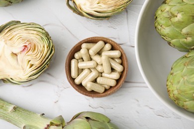 Photo of Bowl with pills and fresh artichokes on white textured table, flat lay