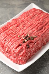 Photo of Raw ground meat and peppercorns on grey table, closeup