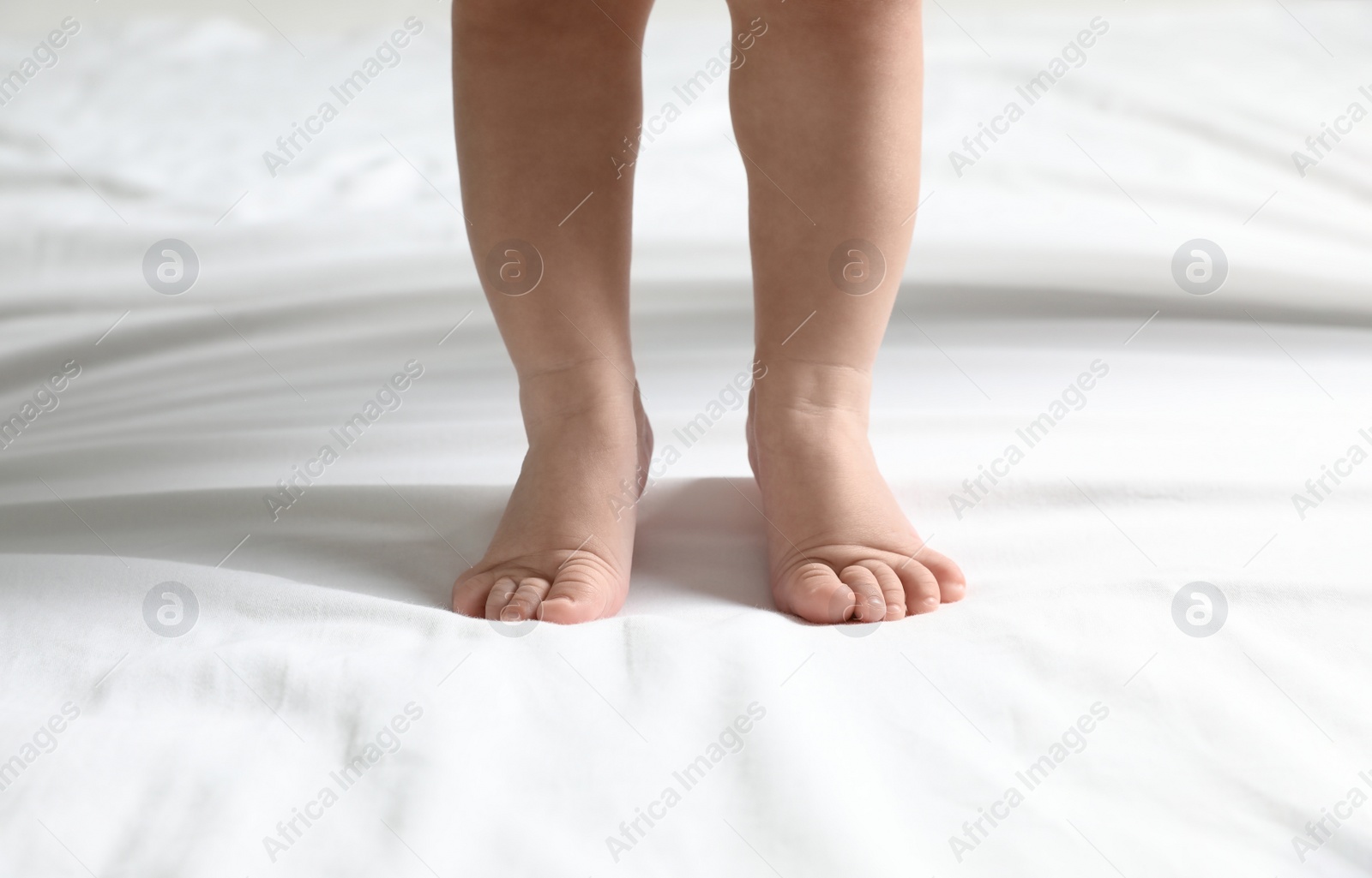 Photo of Cute little baby standing on white bed sheet, closeup