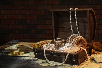 Photo of Chest with treasures and scattered sand on wooden floor, space for text