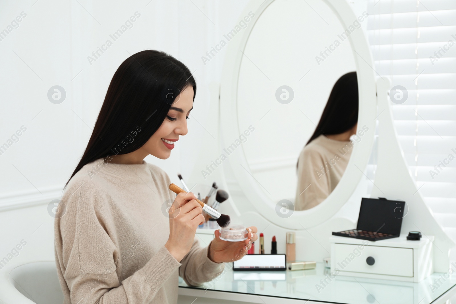 Photo of Beautiful woman applying makeup near mirror in room