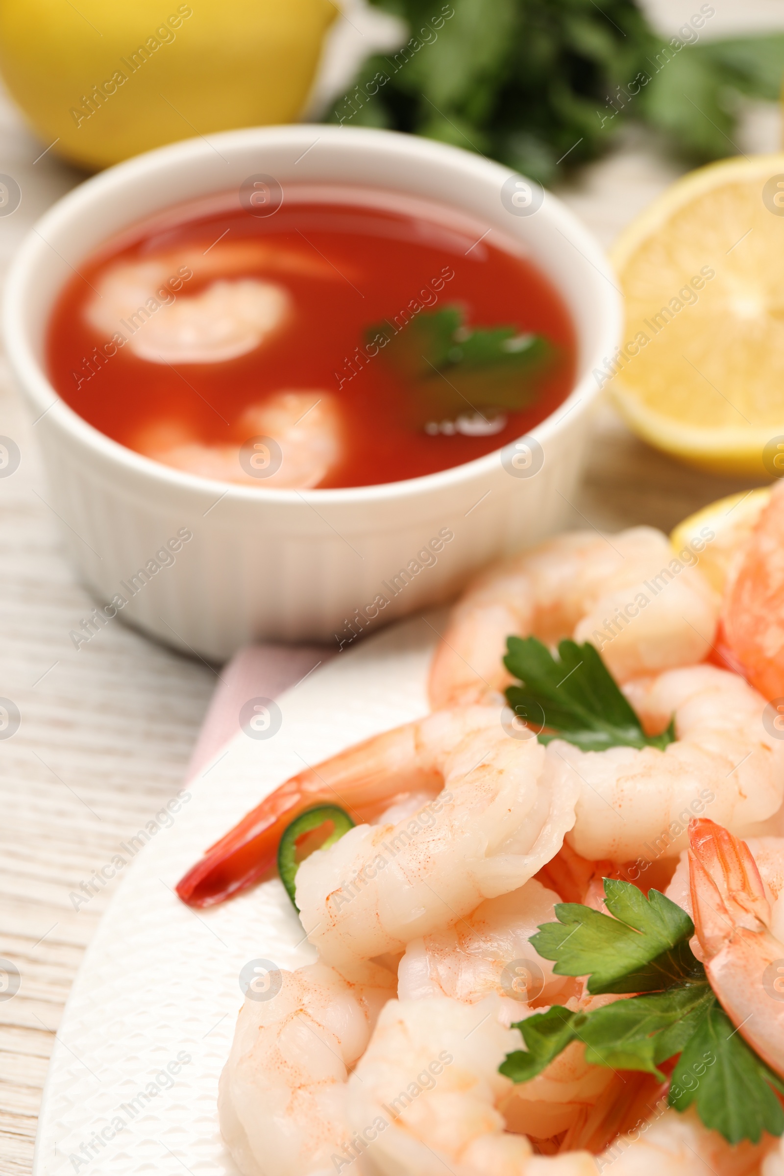 Photo of Tasty boiled shrimps with cocktail sauce, chili and parsley on table, closeup