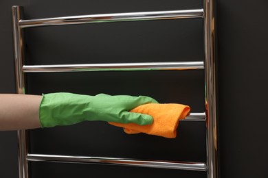 Photo of Woman cleaning heated towel rail with rag, closeup