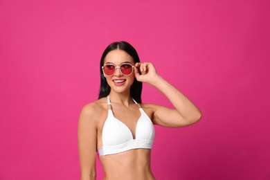 Photo of Beautiful young woman in white bikini with sunglasses on pink background