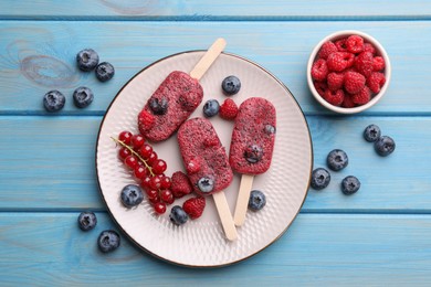 Photo of Plate of tasty berry ice pops on light blue wooden table, flat lay. Fruit popsicle
