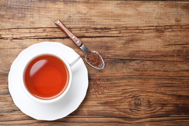 Photo of Freshly brewed rooibos tea, dry leaves and spoon on wooden table, flat lay. Space for text